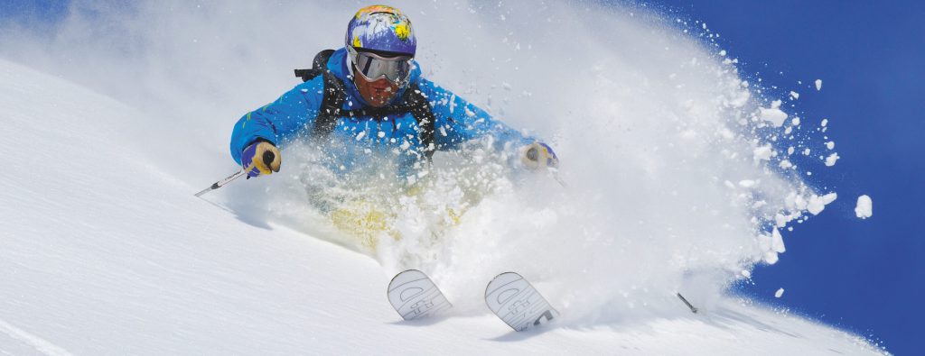 Skifahrer im Tiefschnee mit aufstiebender Schneewolke